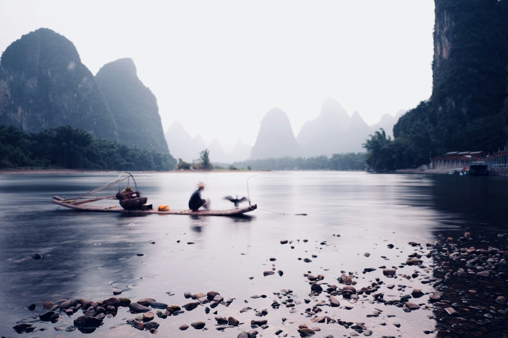 Ein Kormoranfischer auf einem Floß auf dem Li-Fluss unter Karstgipfeln bei Guilin