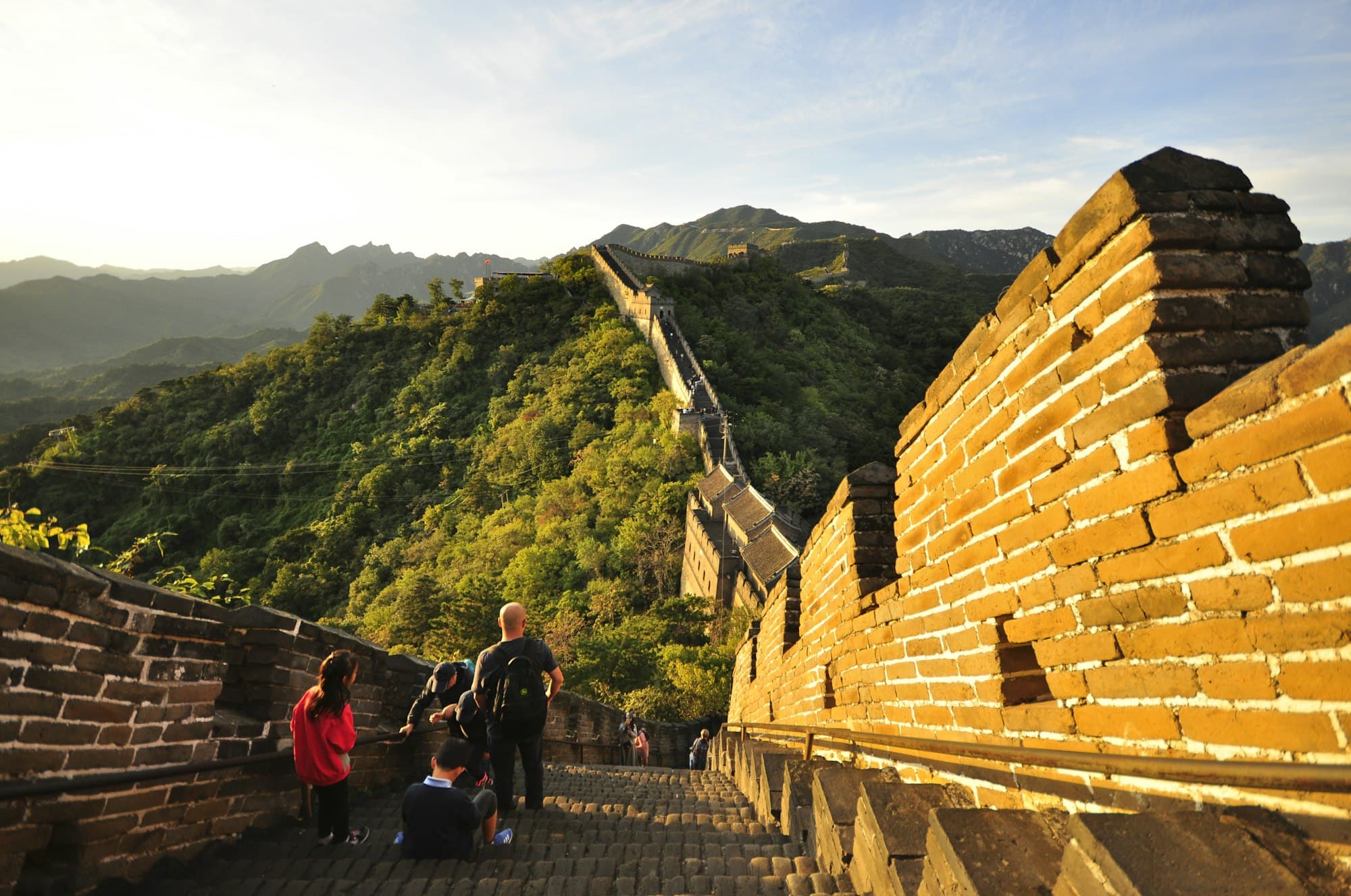 Eine Familie steigt bei goldenem Abendlicht auf einem restaurierten Abschnitt der Chinesischen Mauer bei Peking auf, von hinten gesehen