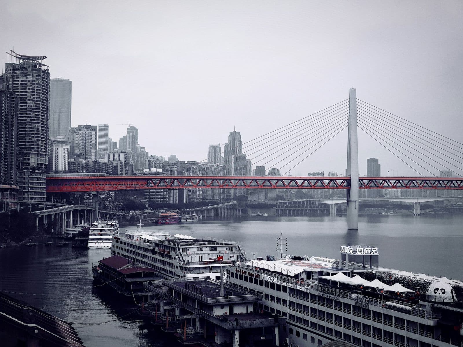 Navi fluviali ormeggiate ai moli di Chaotianmen a Chongqing, con un ponte rosso sul fiume sullo sfondo