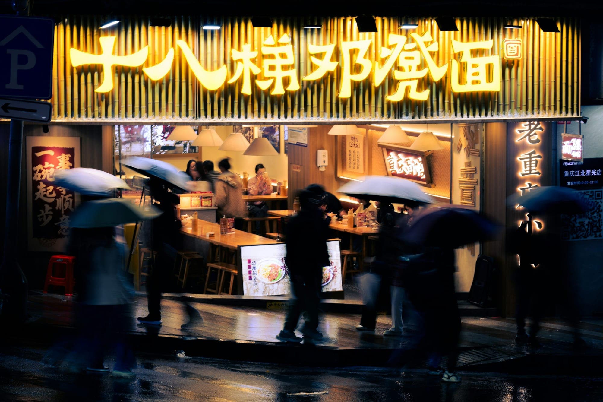 Des personnes avec des parapluies passent devant une échoppe de nouilles un soir de pluie à Chongqing
