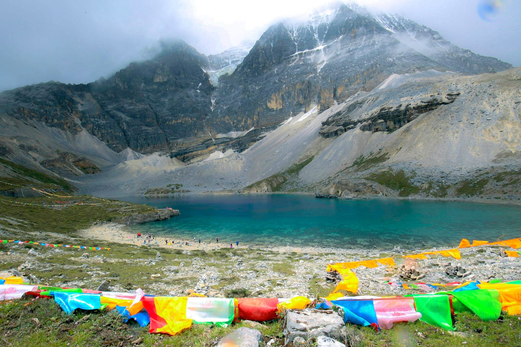 Un lago glaciar bajo picos nevados, con banderas de oración, en Yading, Sichuan