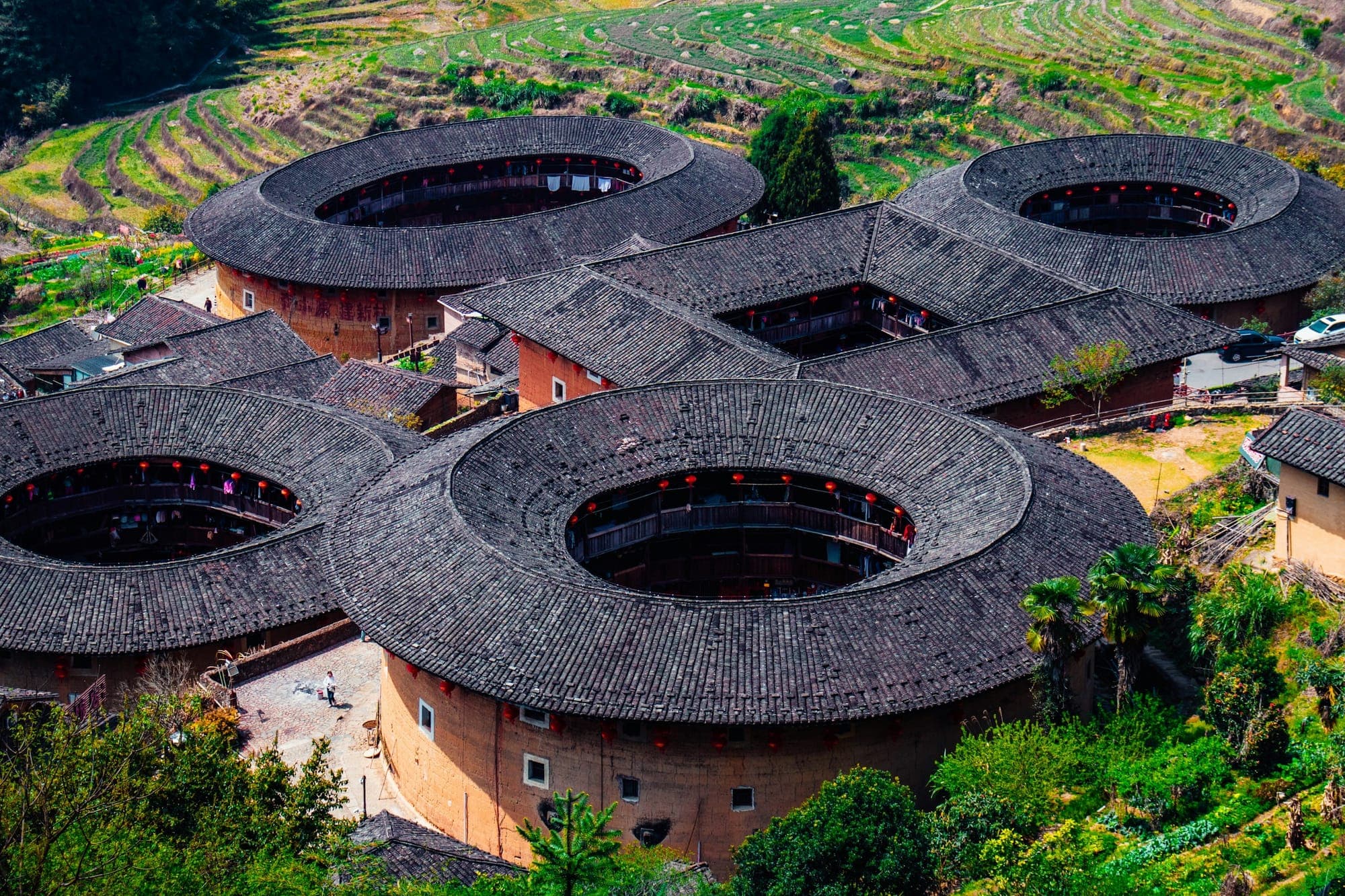 Vista aerea di edifici tulou circolari in terra cruda tra terrazze verdi