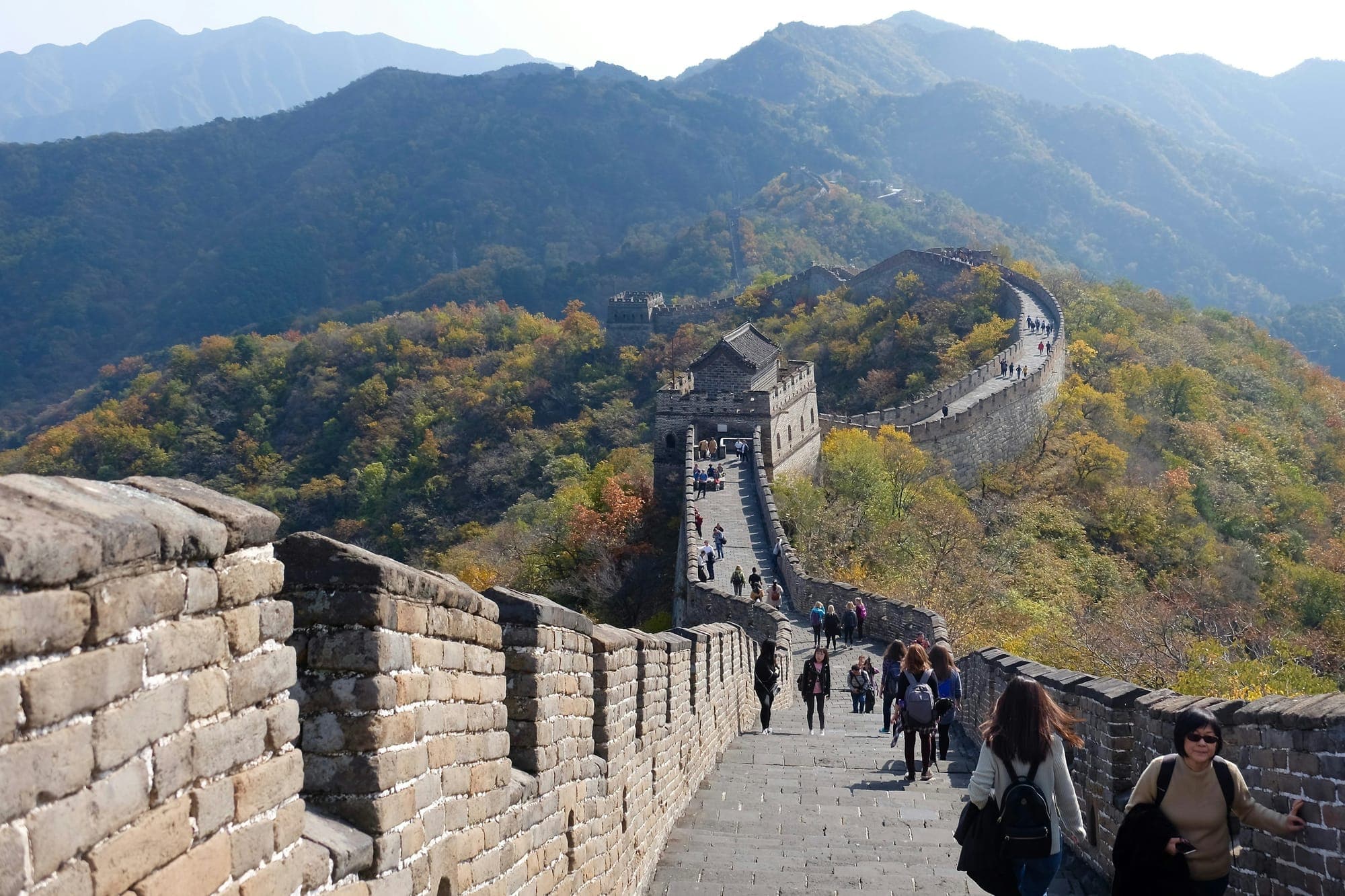 Viaggiatori percorrono una sezione restaurata della Grande Muraglia cinese in una giornata serena