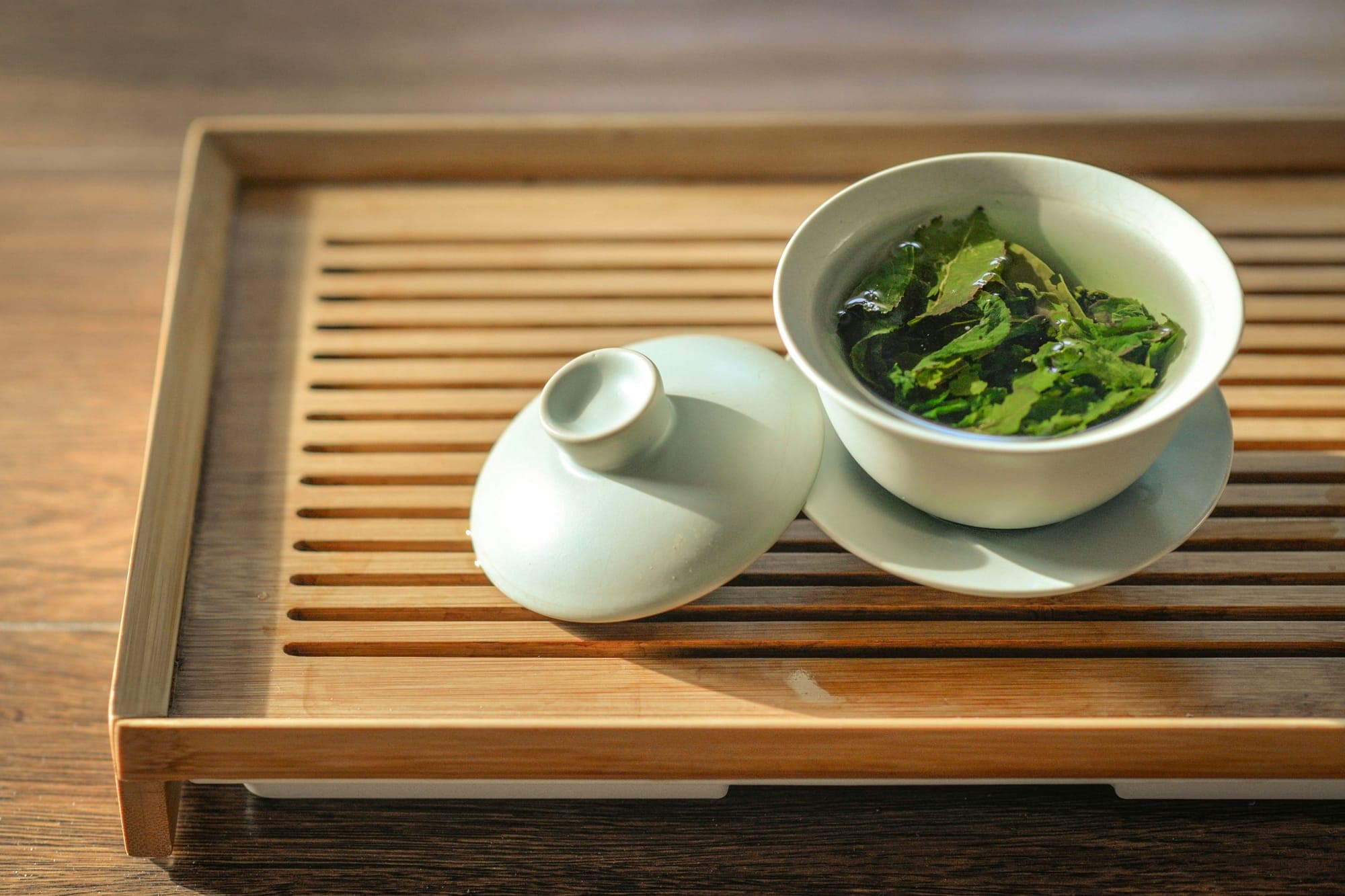 Foglie di tè verde in infusione in un gaiwan bianco su un vassoio di bambù