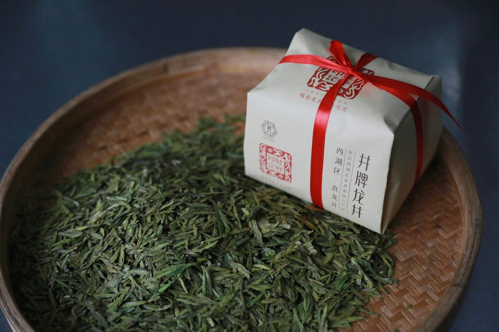 Feuilles de thé vert Longjing plates dans un panier en bambou à côté d’un paquet de thé emballé