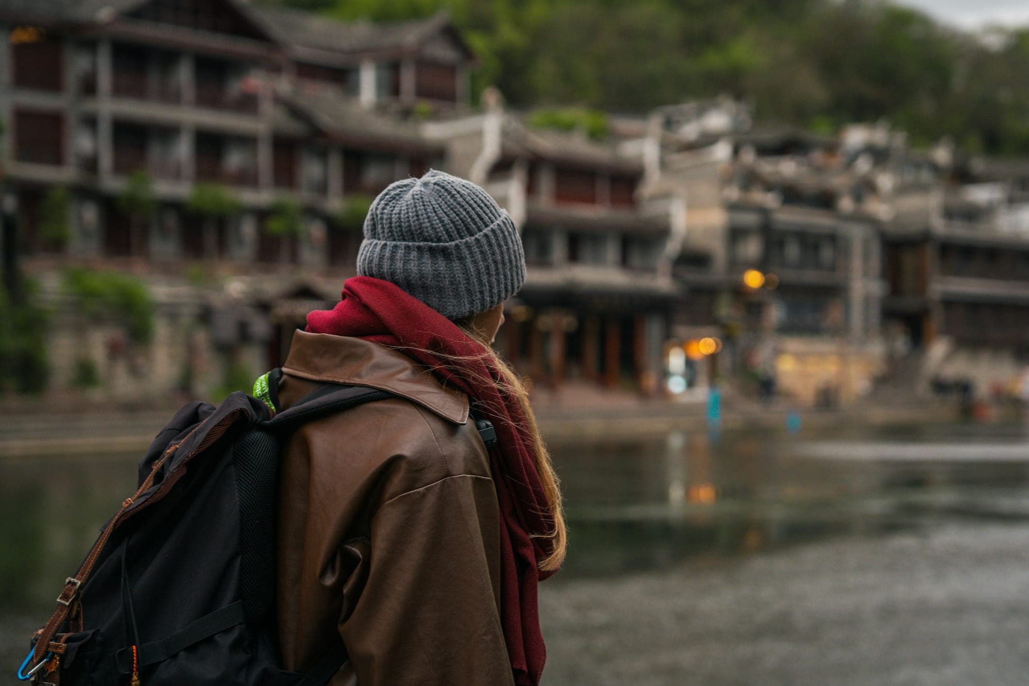 Una viaggiatrice con uno zaino guarda la città vecchia di Fenghuang, Hunan, dall'altra sponda del fiume