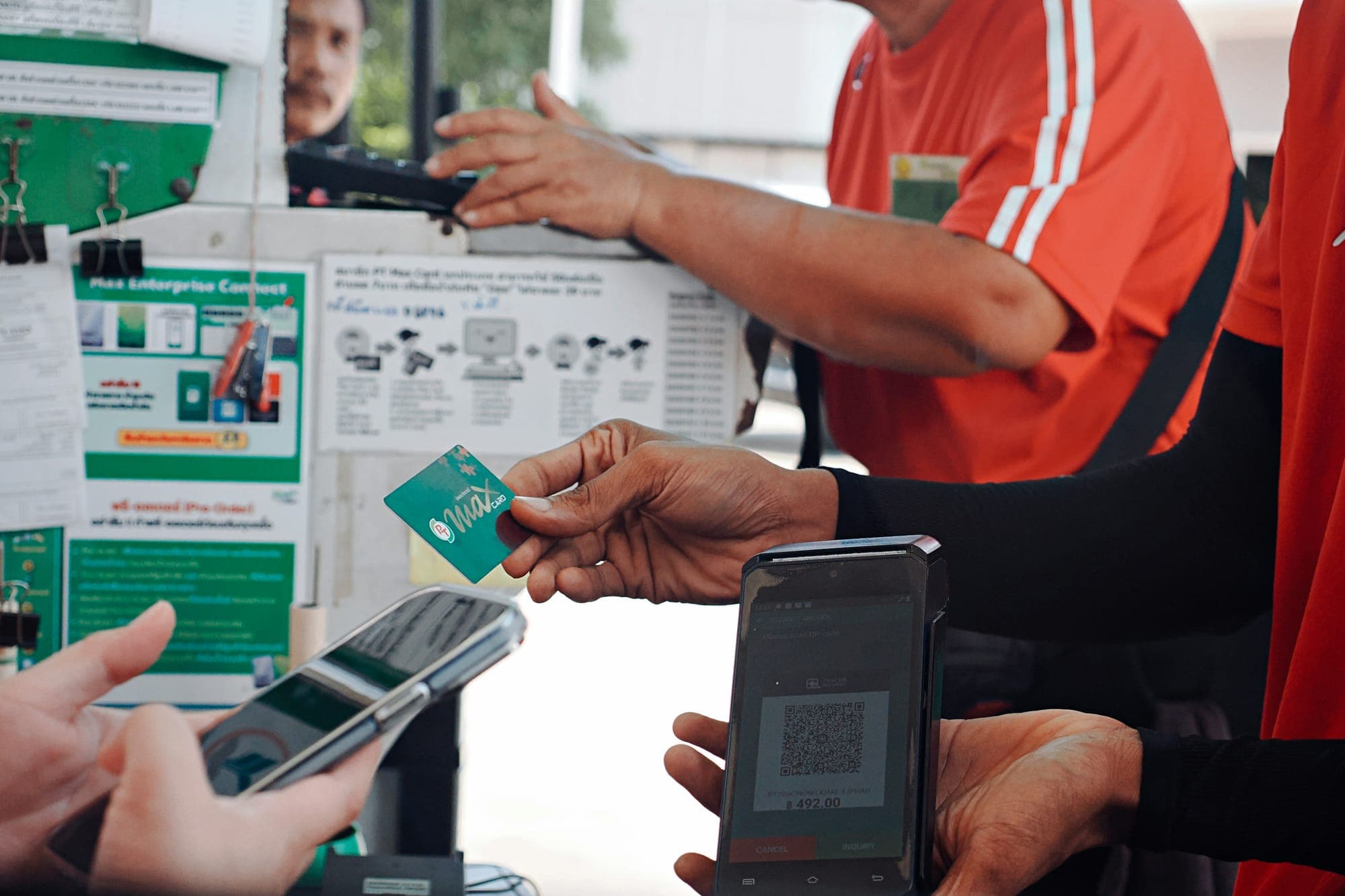 Eine Kundin oder ein Kunde bezahlt an der Ladentheke per QR-Code auf dem Smartphone und hält dabei eine Bankkarte in der Hand