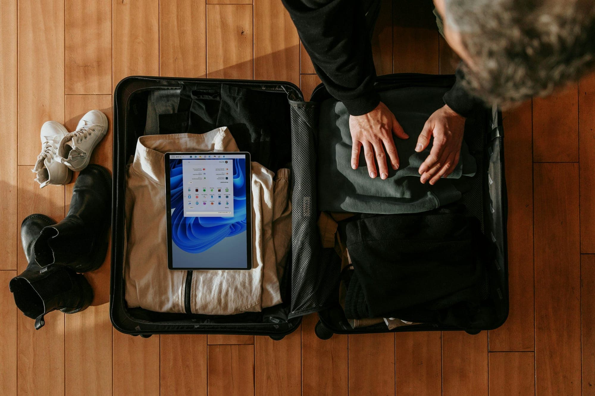 Hände packen Kleidung und ein Tablet in einen offenen Koffer