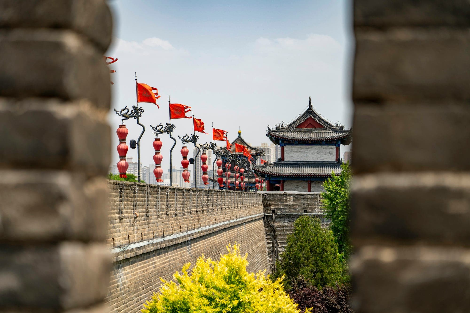 Blick durch eine Zinnenöffnung entlang der Stadtmauer von Xi'an auf einen Torturm mit roten Laternen