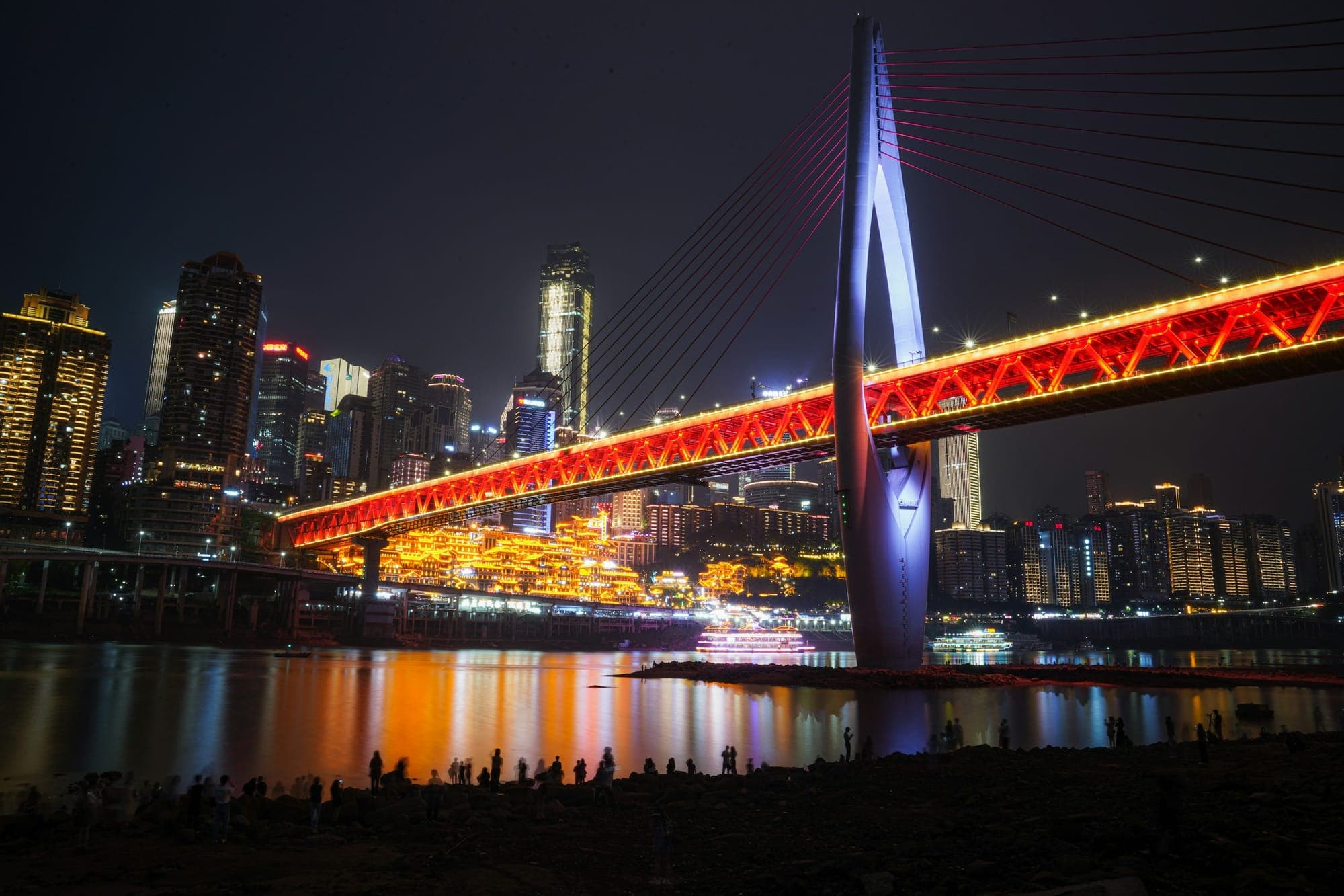 Die Qiansimen Bridge leuchtet nachts rot über dem Fluss in Chongqing – ein echtes Nachtbild der Bergstadt, das online häufig als Cyberpunk bezeichnet wird