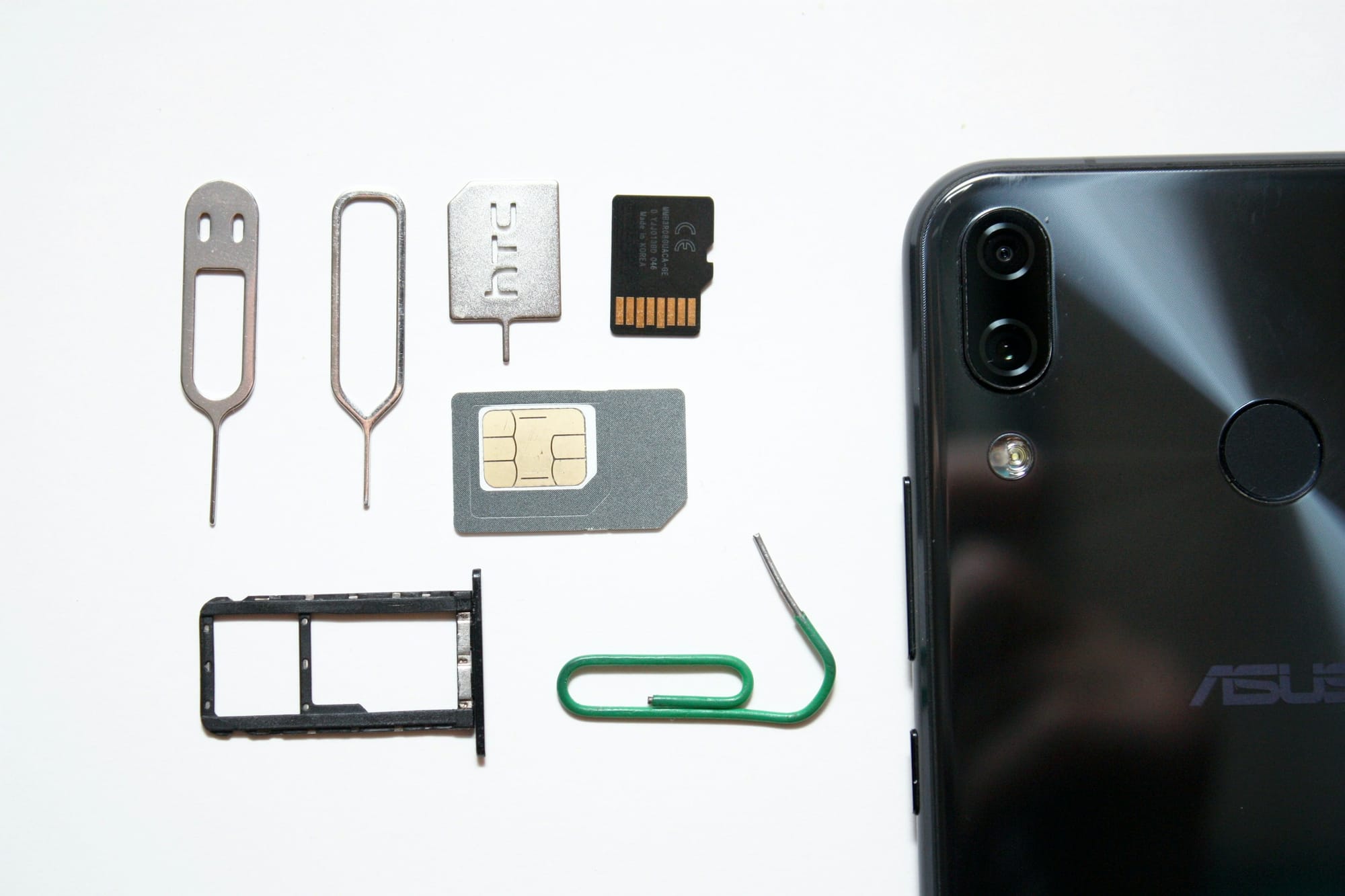 A SIM card, SIM tray and ejector pins beside a smartphone