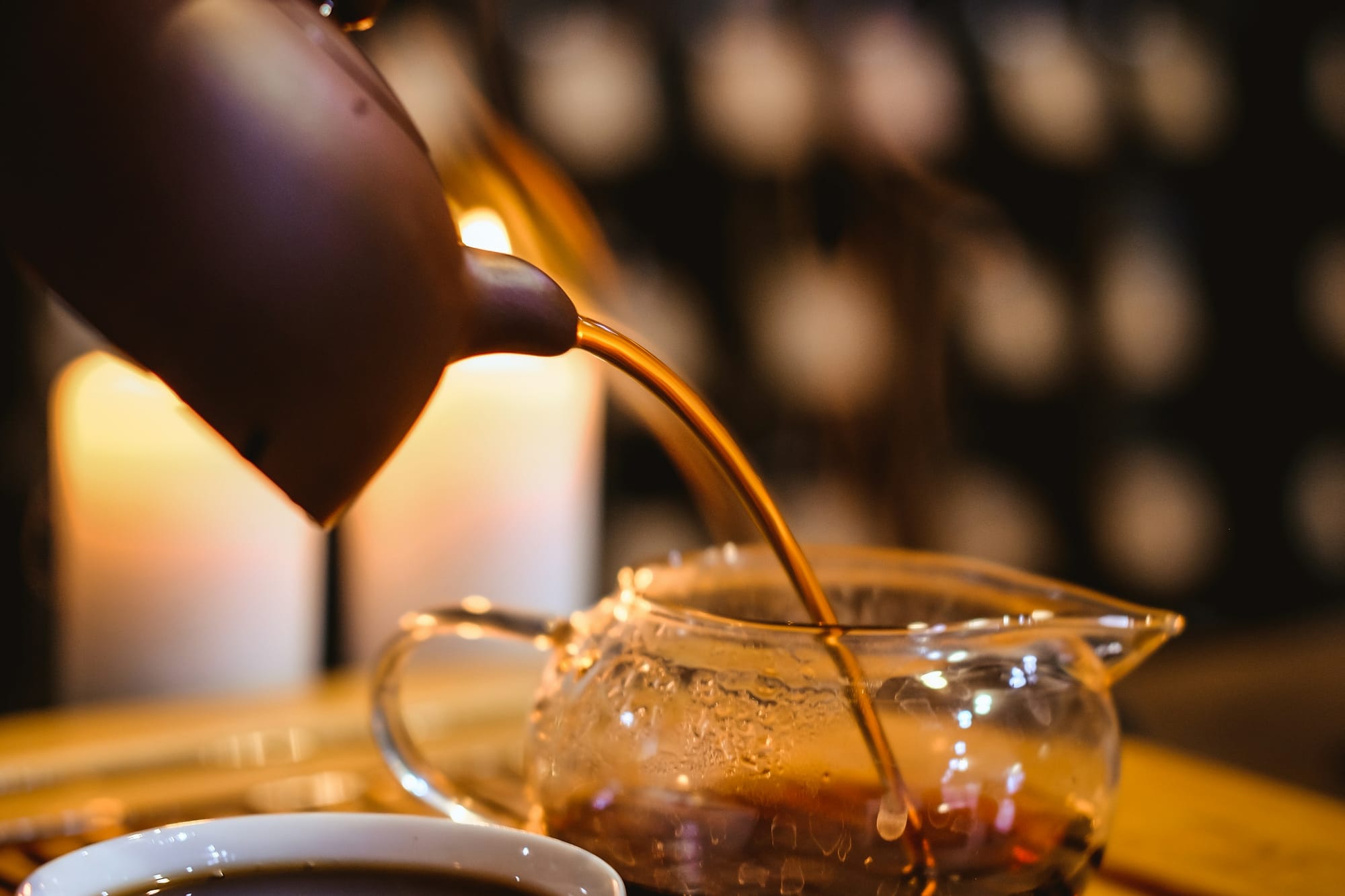 Té ámbar vertido de una tetera de arcilla a una jarra de vidrio