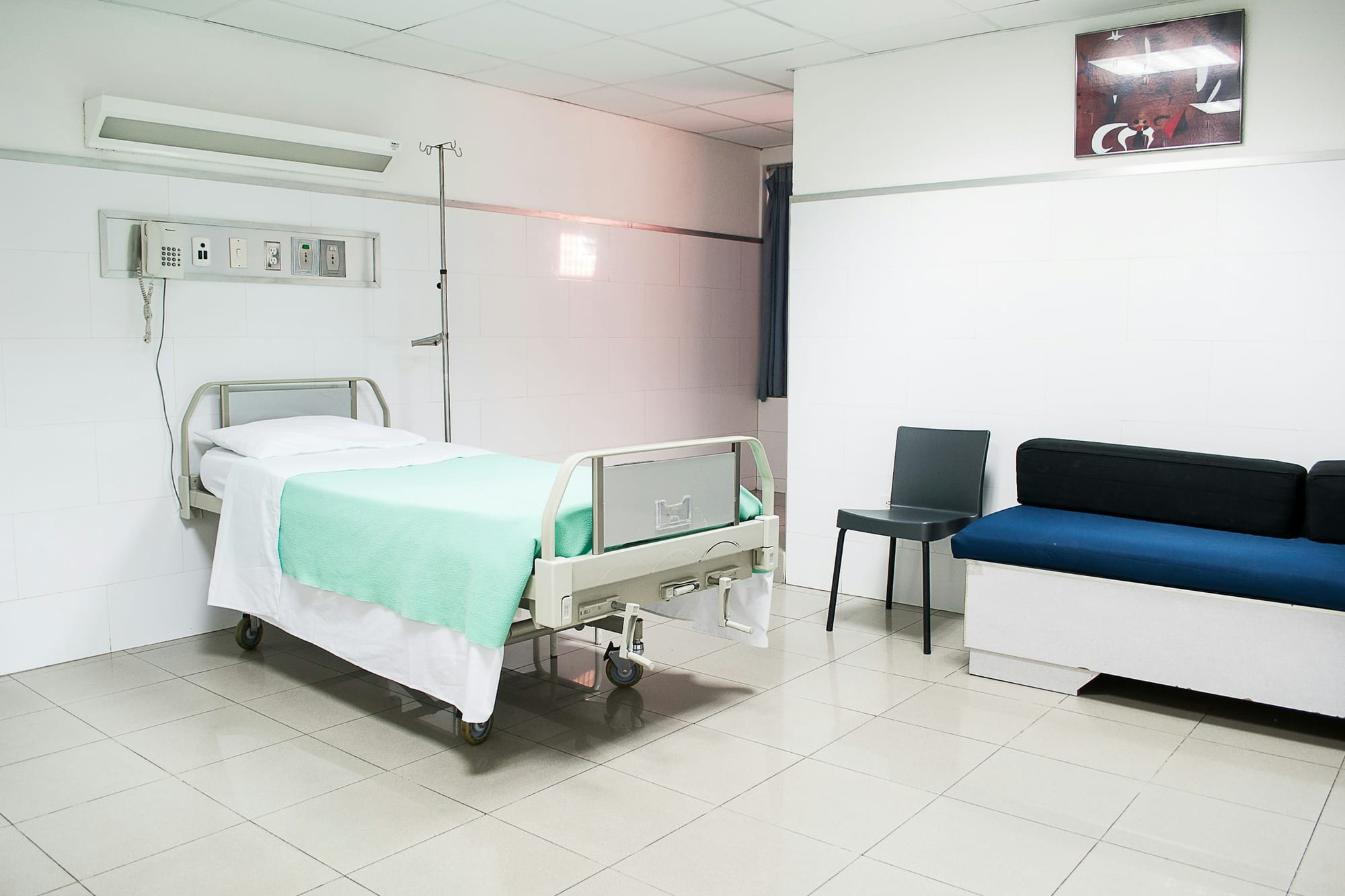 Una stanza d'ospedale con un letto e un divano per i visitatori
