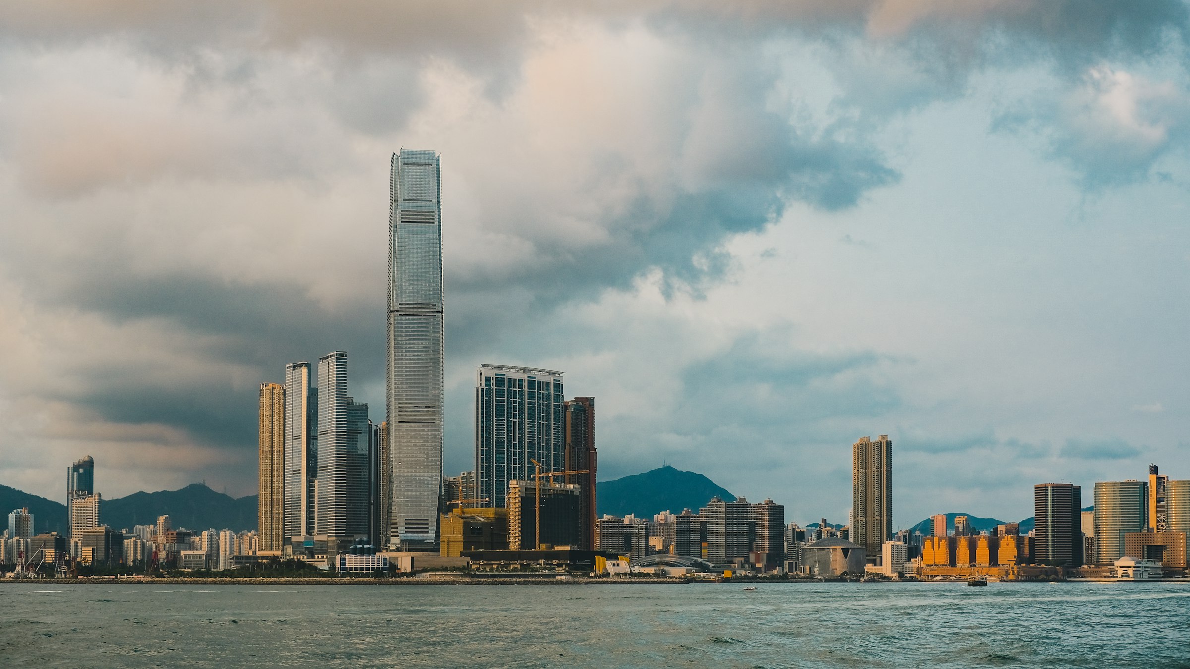 Victoria Harbour and the West Kowloon skyline in Hong Kong SAR under a cloudy sky, photographed from the water